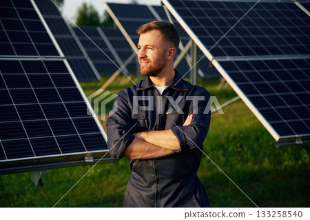 Portrait, standing with arms crossed. Man is working with solar panels outdoors at daytime Portrait, standing with arms crossed. Man is working with solar panels outdoors at daytime 133258540