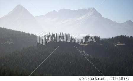 Higher peaks tower over lush forests, bathed in soft morning light. The tranquil scene captures natures beauty, inviting exploration and reflection amidst the grandeur of the wilderness. 133258572