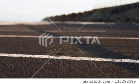 The scene captures a deserted road by the ocean, showcasing a quiet atmosphere. Gentle waves can be seen in the background, hinting at the serene beauty of twilight. 133258589
