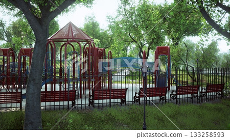 Bright playground filled with red climbing equipment and blue slides surrounded by lush green trees. Wooden benches line the path, inviting relaxation in a peaceful park atmosphere. 133258593