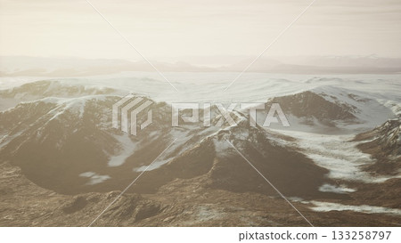 Snow capped peaks rise majestically in a serene landscape bathed in soft sunlight. The vast expanse stretches far, showcasing natures quiet beauty at dusk. 133258797