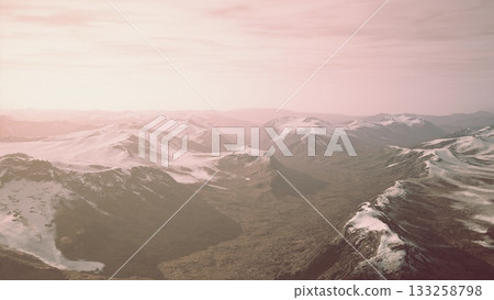 Mountains stretch under a delicate layer of snow as the sunset casts a pink glow over the landscape. Valleys below reveal rich hues and vastness, inviting exploration and wonder. Mountains stretch under a delicate layer of snow as the sunset casts a pink glow over the landscape. Valleys below reveal rich hues and vastness, inviting exploration and wonder. 133258798