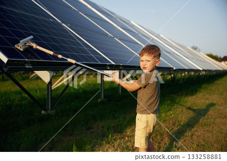 Busy by cleaning the surface. Little boy is with solar panels outdoors 133258881