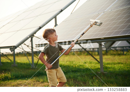 Busy by cleaning the surface. Little boy is with solar panels outdoors 133258883