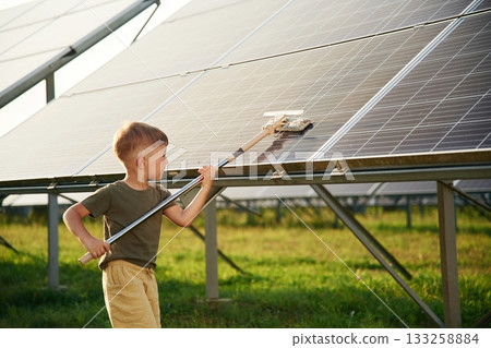 Busy by cleaning the surface. Little boy is with solar panels outdoors Busy by cleaning the surface. Little boy is with solar panels outdoors 133258884