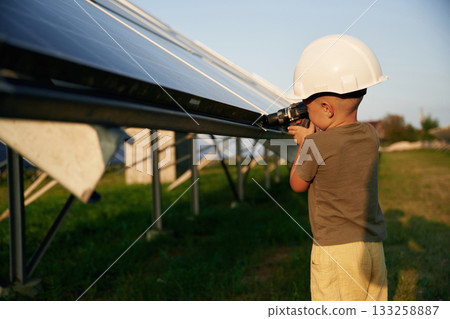 Doing repairs by using drill. Little boy is with solar panels outdoors Doing repairs by using drill. Little boy is with solar panels outdoors 133258887