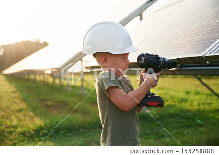 Doing repairs by using drill. Little boy is with solar panels outdoors Doing repairs by using drill. Little boy is with solar panels outdoors 133258888
