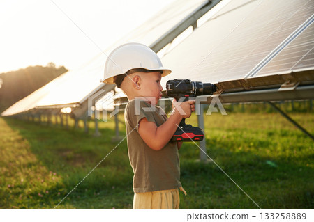 Doing repairs by using drill. Little boy is with solar panels outdoors Doing repairs by using drill. Little boy is with solar panels outdoors 133258889