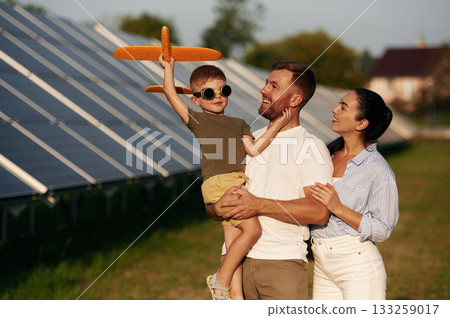 Leisure, with toy plane. Father, mother and little son are outdoors near solar panels Leisure, with toy plane. Father, mother and little son are outdoors near solar panels 133259017