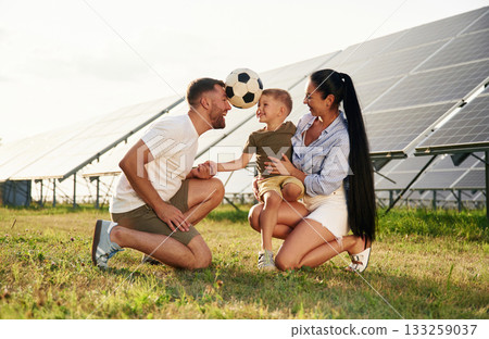 Rural scene, with soccer ball. Father, mother and little son are outdoors near solar panels Rural scene, with soccer ball. Father, mother and little son are outdoors near solar panels 133259037