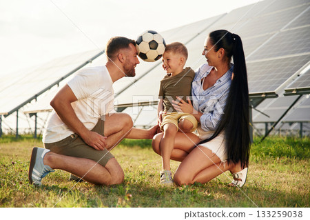 Rural scene, with soccer ball. Father, mother and little son are outdoors near solar panels Rural scene, with soccer ball. Father, mother and little son are outdoors near solar panels 133259038