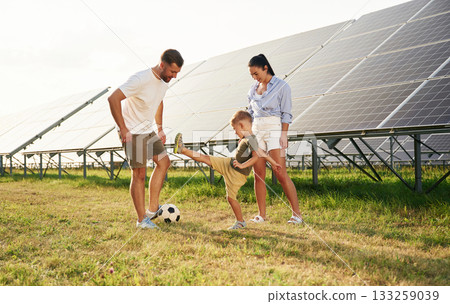 Rural scene, with soccer ball. Father, mother and little son are outdoors near solar panels Rural scene, with soccer ball. Father, mother and little son are outdoors near solar panels 133259039