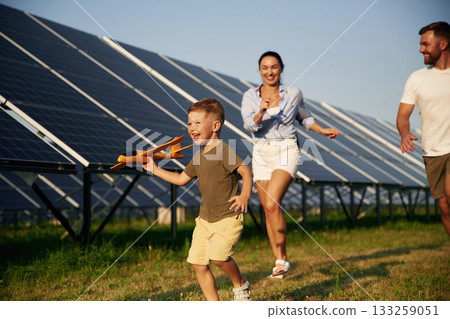 Boy is running with toy plane. Father, mother and little son are outdoors near solar panels Boy is running with toy plane. Father, mother and little son are outdoors near solar panels 133259051