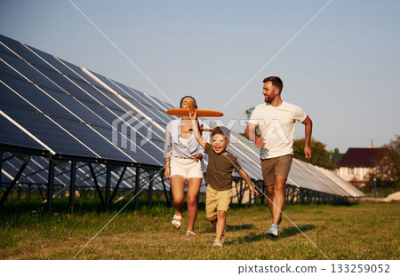 Boy is running with toy plane. Father, mother and little son are outdoors near solar panels 133259052