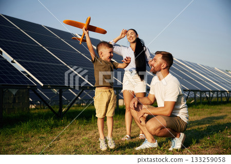 Imagination conception, with toy plane. Father, mother and little son are outdoors near solar panels Imagination conception, with toy plane. Father, mother and little son are outdoors near solar panels 133259058