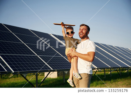 Toy plane in hand. Father with his little son are together near the solar panels Toy plane in hand. Father with his little son are together near the solar panels 133259176