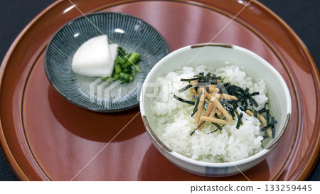 A bowl of nori chazuke (rice with green tea) and a small dish of pickles on a brown round tray 133259445