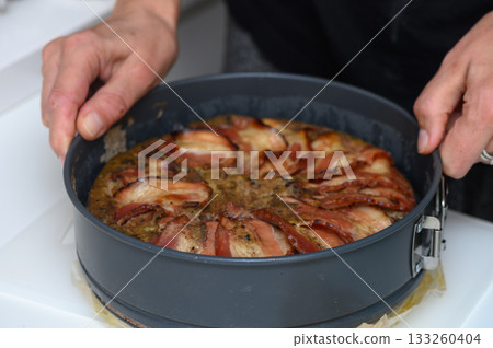 Savory bacon-topped dish being carefully removed from a baking pan in a cozy kitchen setting 133260404