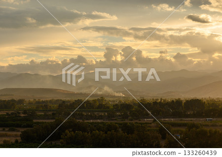 Majestic sunset casts golden hues over rolling hills and serene landscape in the evening light 133260439