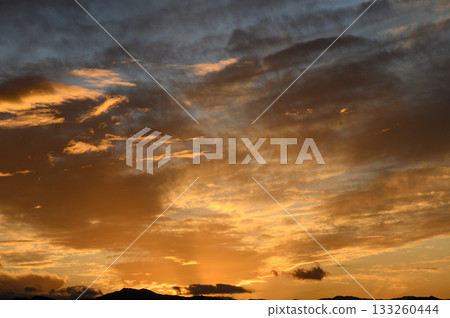 Majestic sunset casts golden hues over the tranquil horizon with clouds in brilliant display 133260444