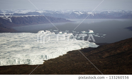 Majestic glaciers flow down rocky slopes, merging with calm waters. Mountains tower in the background under a clear sky, highlighting natures beauty and fragility at this remote Arctic location. Majestic glaciers flow down rocky slopes, merging with calm waters. Mountains tower in the background under a clear sky, highlighting natures beauty and fragility at this remote Arctic location. 133260556