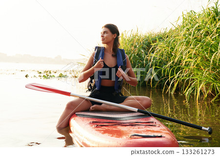 Plants growing on the side. Young woman is with the sup board on the lake 133261273