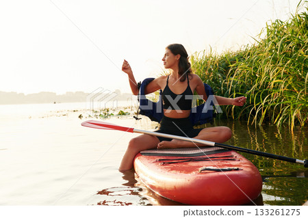 Plants growing on the side. Young woman is with the sup board on the lake 133261275