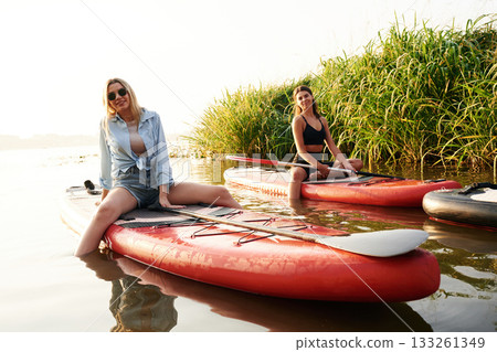 Taking a break. Women friends are on sup board on the lake together Taking a break. Women friends are on sup board on the lake together 133261349