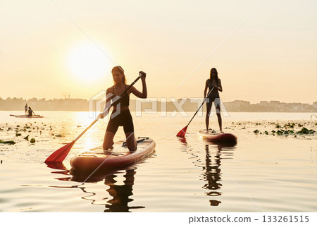 Summertime activities. Women friends are on sup board on the lake together 133261515