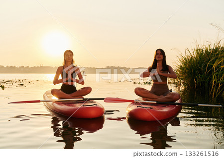 In lotus pose. Women friends are on sup board on the lake together 133261516