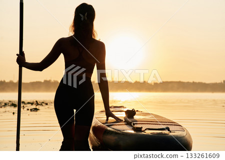 Enjoying the sunset, illuminated. Young woman is with the sup board on the lake Enjoying the sunset, illuminated. Young woman is with the sup board on the lake 133261609