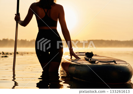 Majestic sunset, standing and looking. Young woman is with the sup board on the lake 133261613