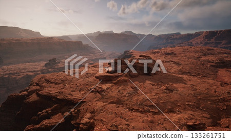 Sunset casts a warm glow over vast rock formations in a desert canyon. The rugged terrain showcases natures beauty as shadows lengthen across the landscape, inviting exploration and wonder. 133261751