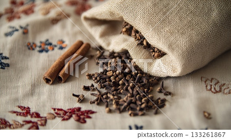 A handmade sachet filled with cloves and cinnamon, lying on embroidered linen. . 133261867