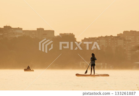 Illuminated by sunlight. Girl kid is on the sup board, on the lake Illuminated by sunlight. Girl kid is on the sup board, on the lake 133261887