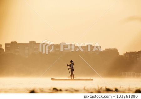Illuminated by sunlight. Girl kid is on the sup board, on the lake Illuminated by sunlight. Girl kid is on the sup board, on the lake 133261890