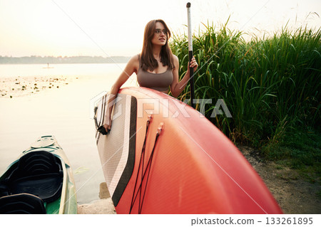 Front view, on the shore. Young woman is with the sup board on the lake Front view, on the shore. Young woman is with the sup board on the lake 133261895