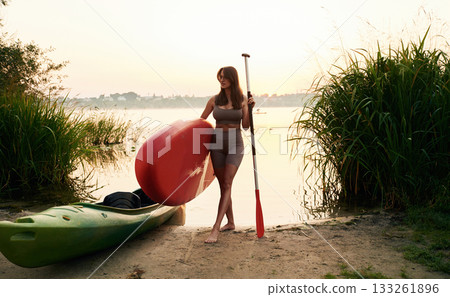 Front view, on the shore. Young woman is with the sup board on the lake 133261896