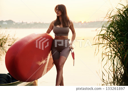 Front view, on the shore. Young woman is with the sup board on the lake 133261897