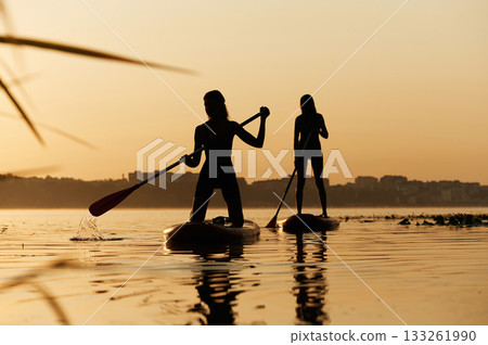 Summertime activities. Women friends are on sup board on the lake together Summertime activities. Women friends are on sup board on the lake together 133261990
