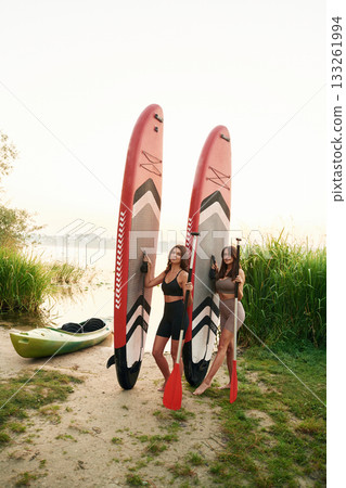 On the shore. Women friends are on sup board on the lake together On the shore. Women friends are on sup board on the lake together 133261994