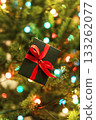 Christmas present on Christmas tree with garland lights , Gift in green box with red ribbon , New Year holidays present 133262077