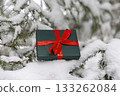 Gift in green box with red ribbon on snowy spruce tree in winter forest Christmas background and New Year holidays 133262084