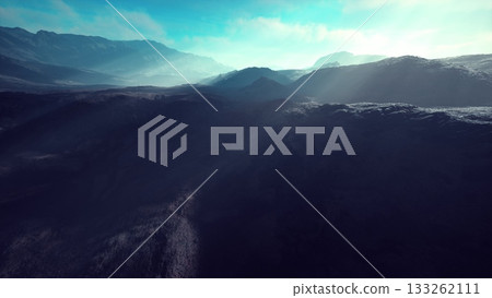 Morning light illuminates a breathtaking mountain range, with mist swirling through the valleys. The vibrant blue sky contrasts with the rugged terrain, creating a serene atmosphere. 133262111