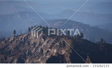 A breathtaking mountain range looms in the distance, enveloped in a gentle mist. Tall trees cling to the rugged peaks, creating an ethereal atmosphere at dawn. A breathtaking mountain range looms in the distance, enveloped in a gentle mist. Tall trees cling to the rugged peaks, creating an ethereal atmosphere at dawn. 133262115