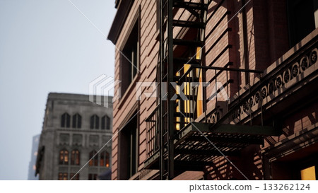 A detailed view of an urban building showcasing intricate architecture and a fire escape. Evening light bathes the structure, highlighting its warm tones and inviting ambiance in a bustling city. 133262124