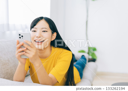 A woman lying on the sofa and using a smartphone 133262194