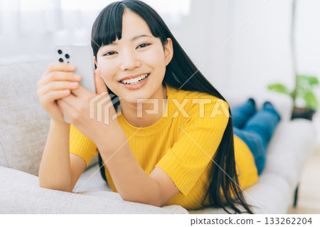 A woman lying on the sofa and using a smartphone A woman lying on the sofa and using a smartphone 133262204