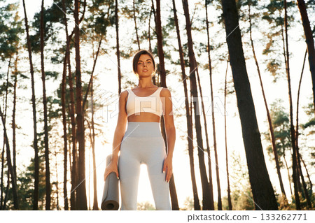 Bright sunlight, holding mat. Woman is doing yoga fitness exercises in the forest 133262771