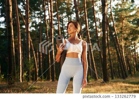 Model is posing with mat in hand. Woman is doing yoga fitness exercises in the forest Model is posing with mat in hand. Woman is doing yoga fitness exercises in the forest 133262779